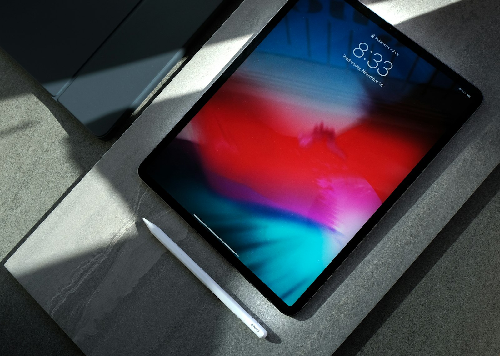 Black iPad with a white stylus on a dark surface