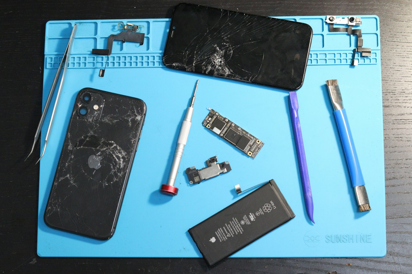 Opened iPhone with a cracked screen, battery and repair tools on a blue repair mat