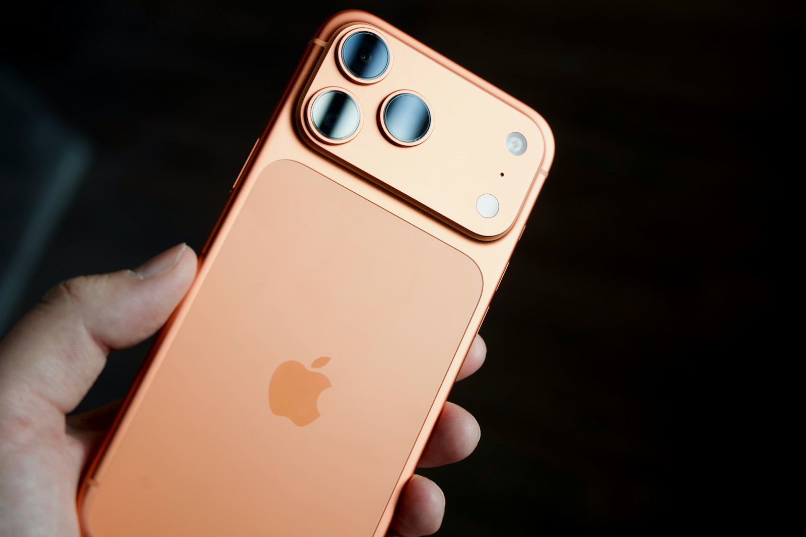 Hand holding a recent orange iPhone Pro with a triple camera