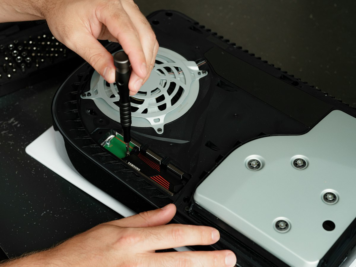 PlayStation 5 with its cover removed while someone works on it with a screwdriver